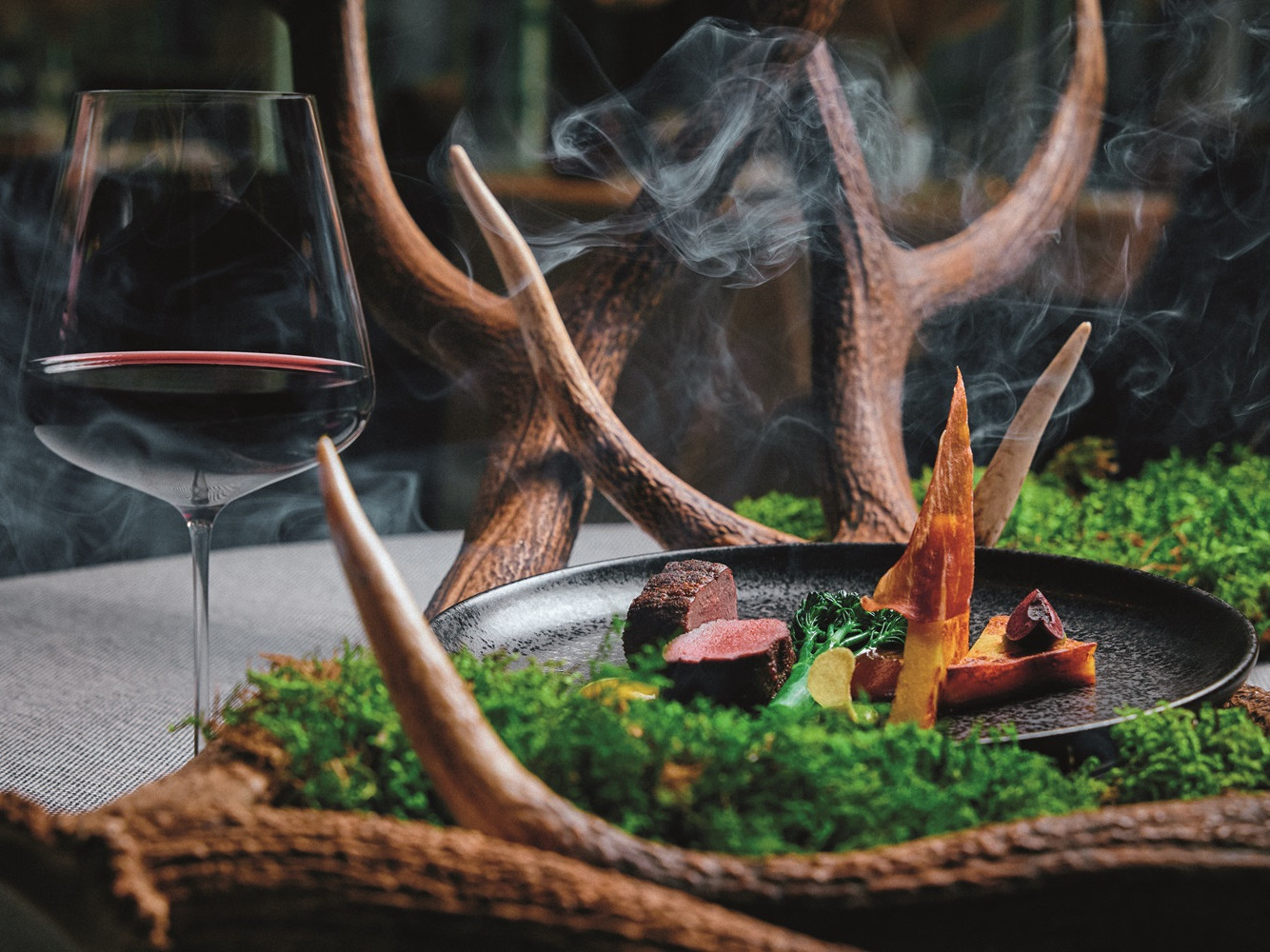 Hirsch im Abendmenü des 5* Wellness- & Sporthotel Jagdhof Ein Teller mit Fleisch und Gemüse neben einem Glas Wein.